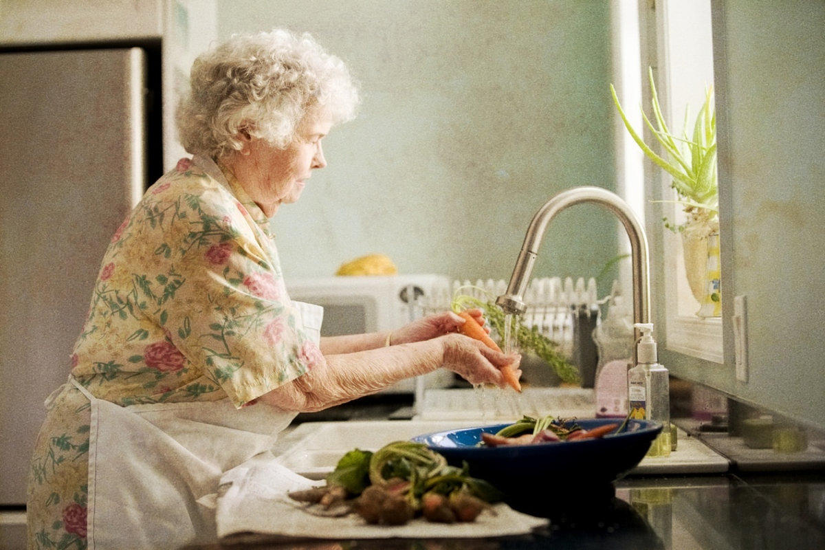 Elderly lady washing carrots at the sink